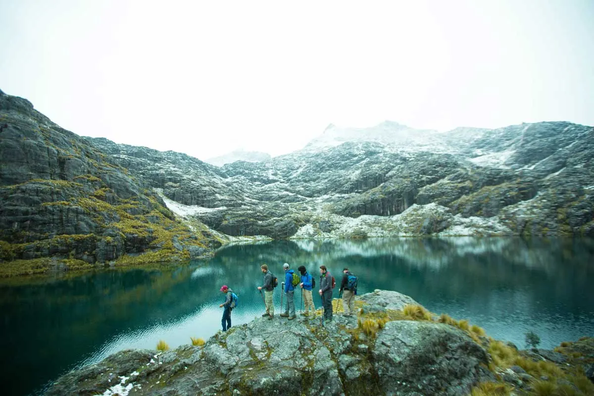 Trekking group beside a glacial lake below snowy mountains