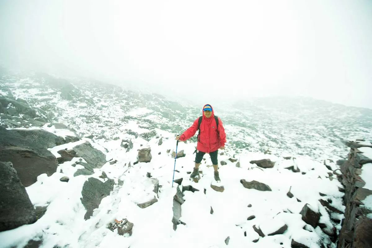 Hiker in a red jacket crossing a snowy pass