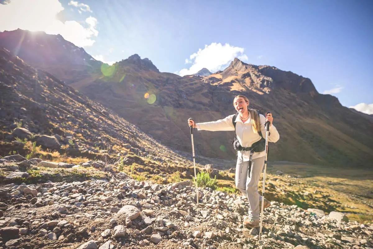 Hiker with trekking poles on a rocky slope in the sun
