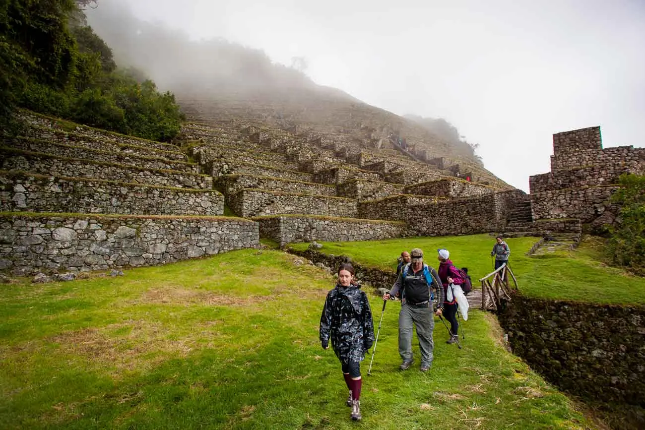 Hikers walking across the terraces of Wiñay Wayna in the mist