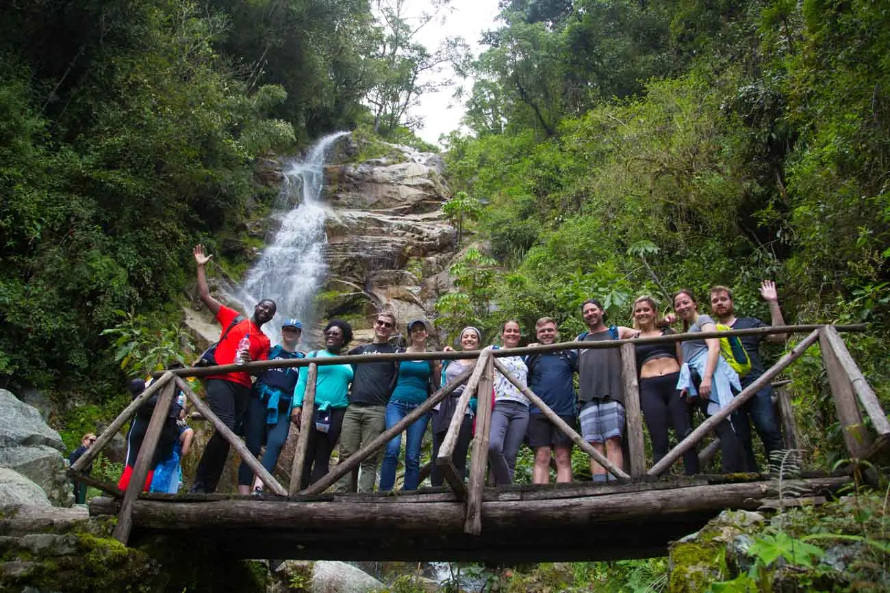 Group on a wooden bridge in front of a waterfall on the way to Wiñay Wayna