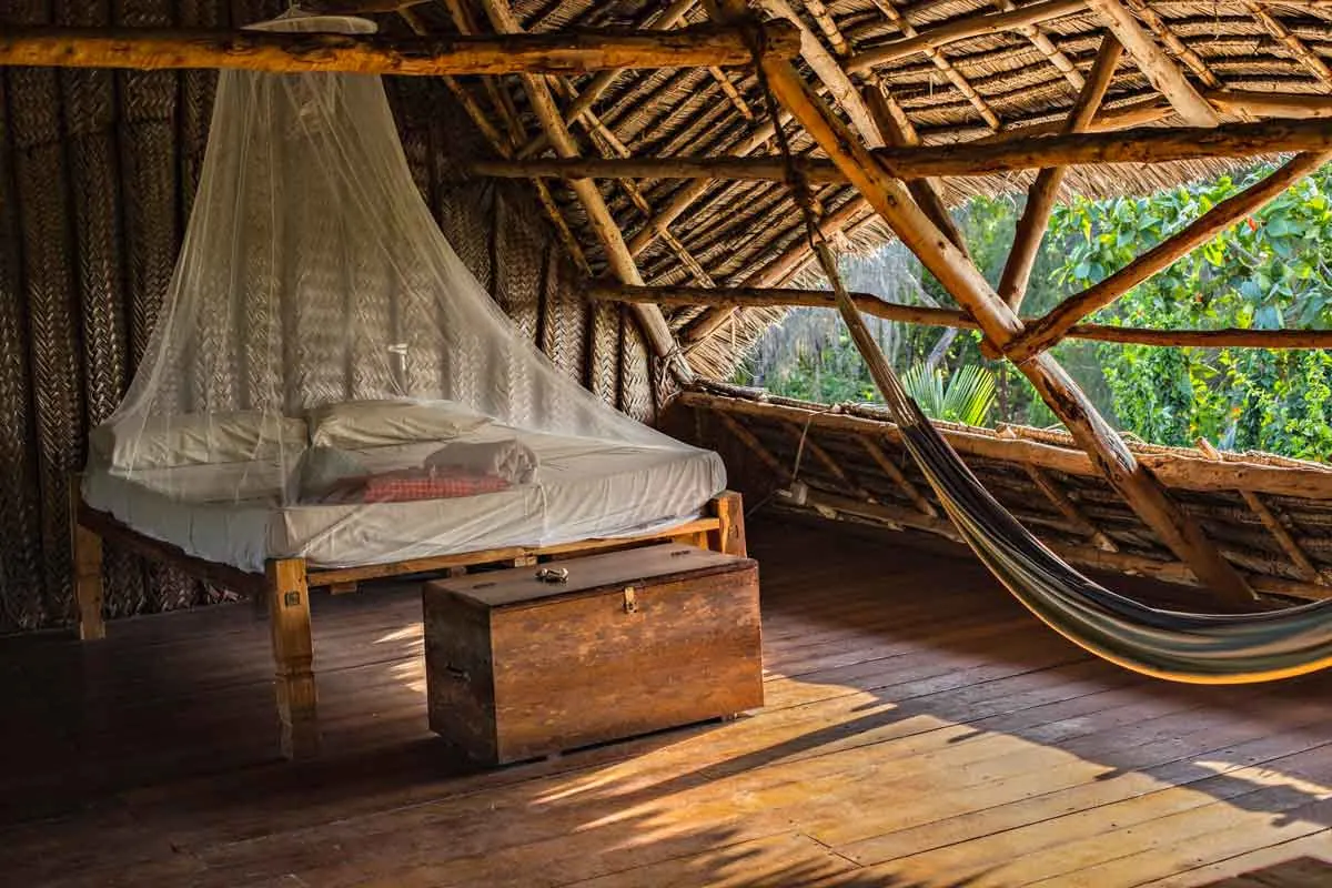 Bed with a mosquito net and a hammock in a wooden lodge
