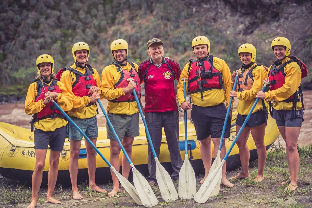 Rafting group in helmets and life jackets holding paddles beside the raft