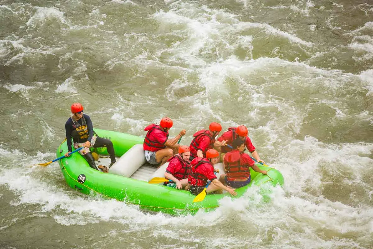 Rafters paddling a green raft through rapids