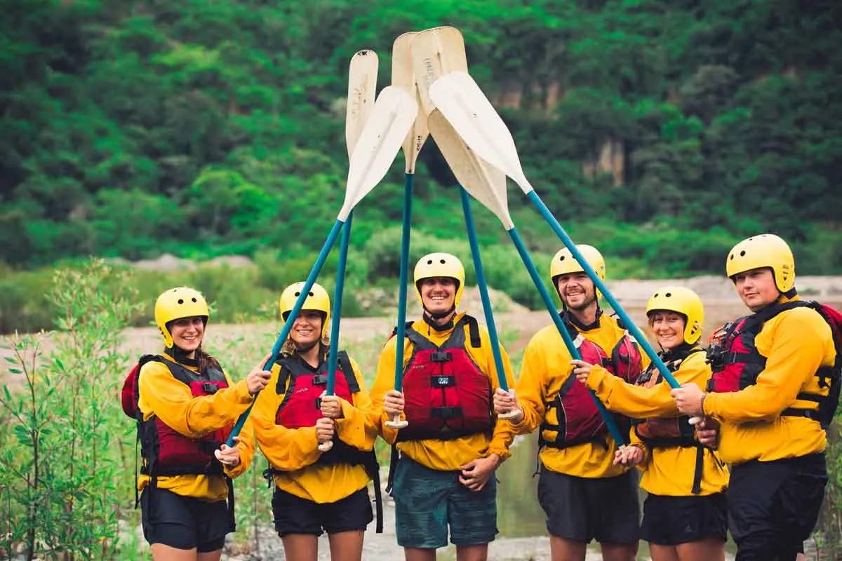 Rafting group in helmets and life jackets raising their paddles